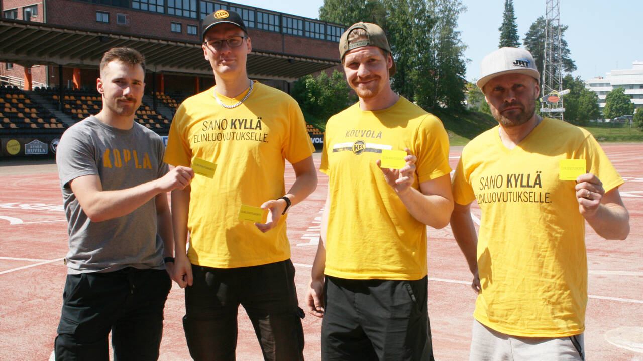 Neljä miestä keltaisissa paidoissa esittelee elinluoutuskorttia